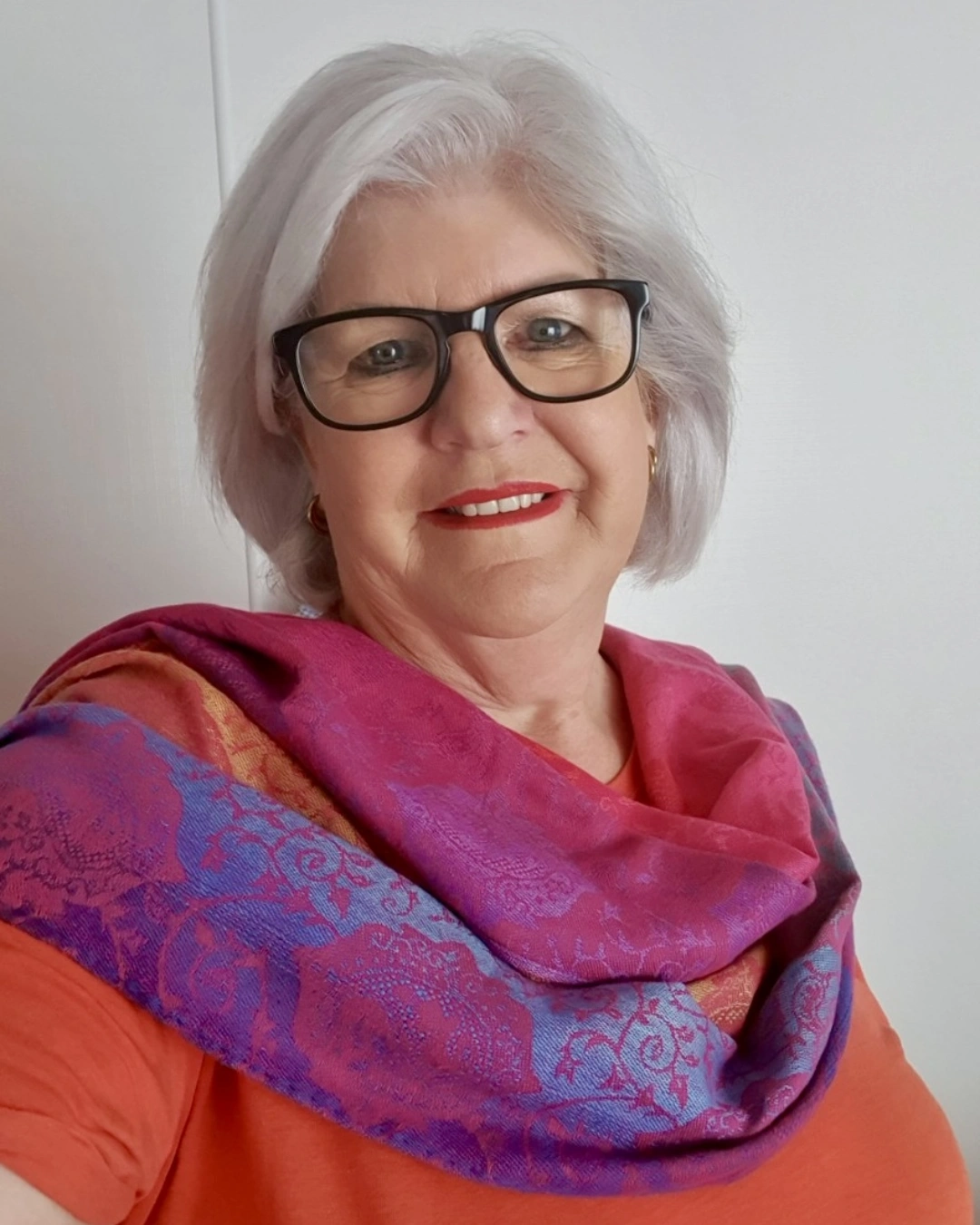 A woman with white hair wearing glasses and a scarf.