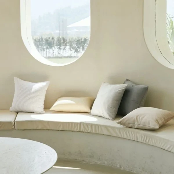 A white couch with pillows in front of a window.