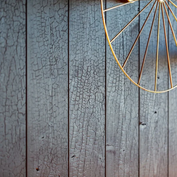 A close up of an old wooden wall with a hanging wheel.