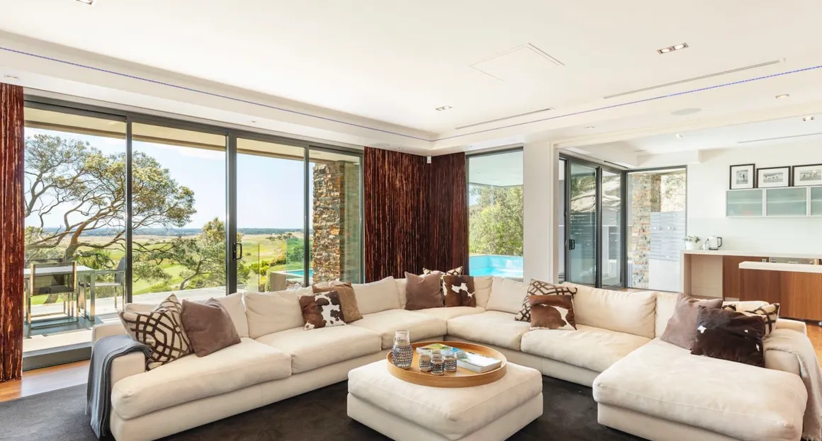 A living room with white furniture and large windows.