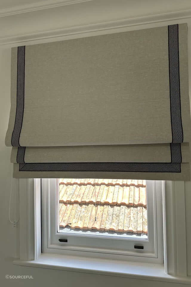 A window with a beige roman shade and grey trim.