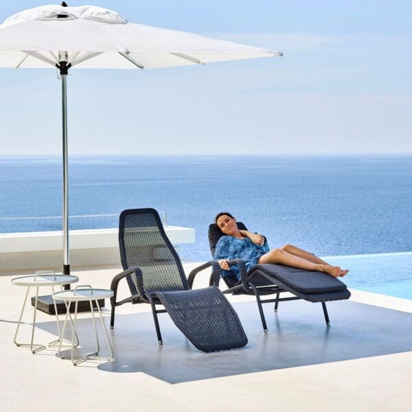 A woman sitting on top of an outdoor chair next to the ocean.