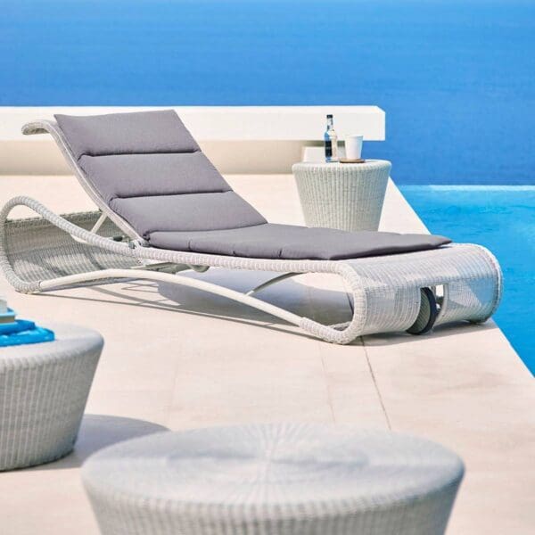 A pool with a lounge chair and table by the water